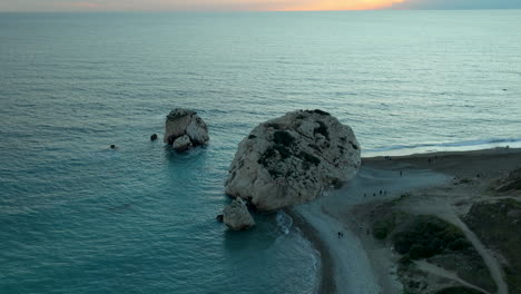 Aphrodite's-Rock-in-Paphos,-aerial-view-during-blue-hour-with-tourists-on-the-coast