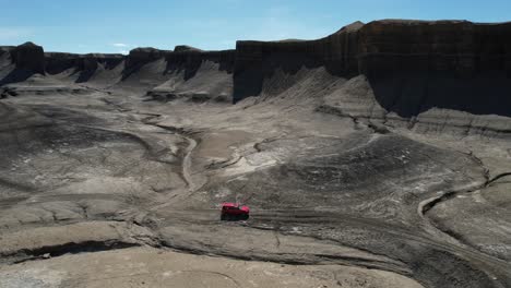 Toma-De-Drone-De-Un-Vehículo-Todoterreno-Rojo-Moviéndose-En-Un-Paisaje-Desértico-Seco-De-Utah,-EE.UU.