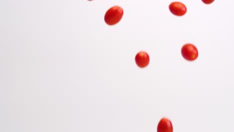 fresh, bright red cherry tomato fruits and vegetables raining down on white backdrop in slow motion