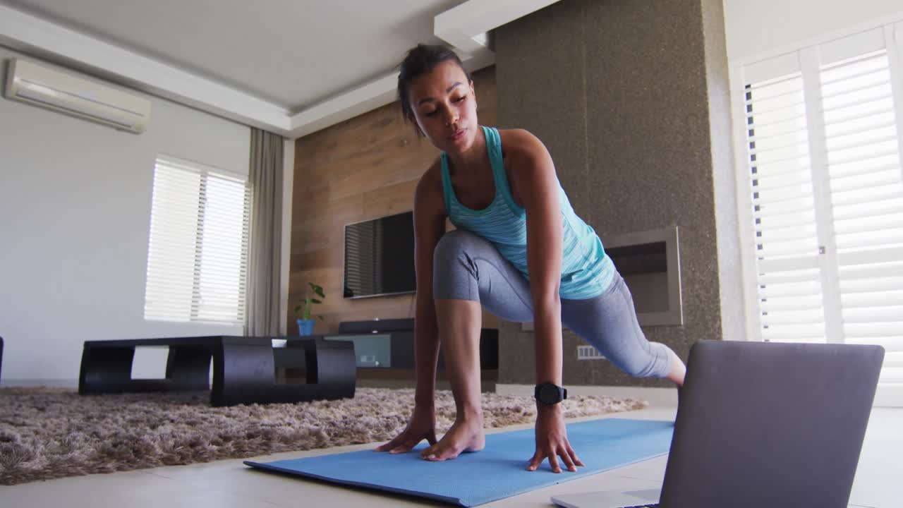 mujer de raza mixta haciendo ejercicio en una alfombra con computadora portátil