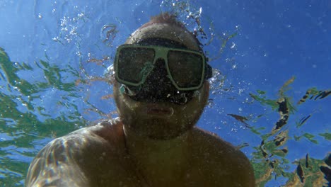 Hombre-Con-Máscara-De-Buceo-En-Agua-De-Mar-Clara-Divertirse-Con-Burbujas-De-Aire-Bajo-El-Agua-De-La-Boca-Durante-Las-Vacaciones-De-Verano