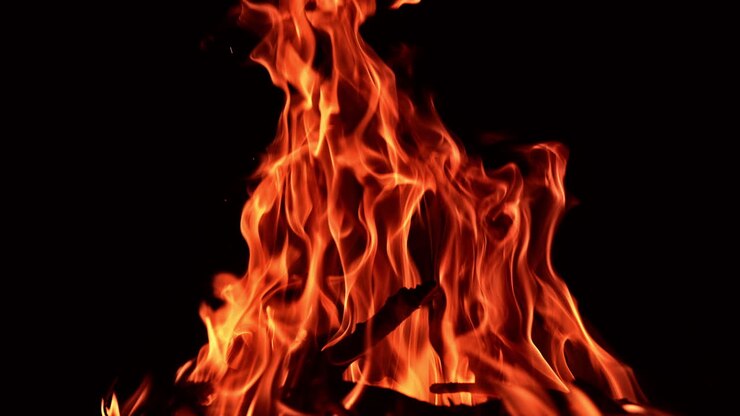 Grande falò che brucia di notte. Bastoni neri bruciano nel falò con fiamma rossa. Primo piano.
