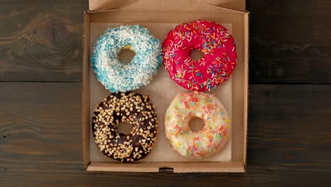 manos femeninas abren caja con rosquillas en fondo de madera