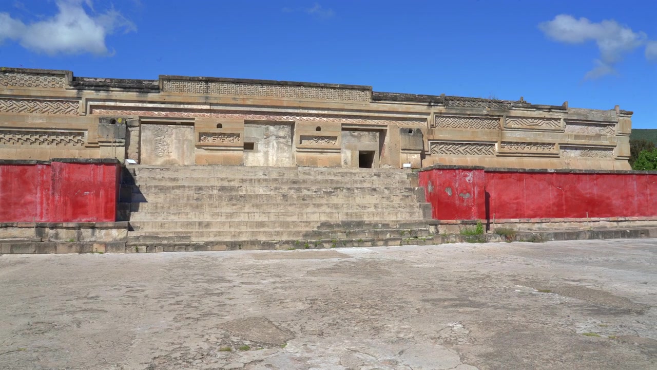 Panoramica ampia della facciata principale del palazzo zapoteco con scale in pietra e muri in stucco rosso presso il sito archeologico di Mitla a Oaxaca, Messico