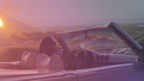 animation of happy biracial woman wearing glasses, driving a cabriolet at sunset