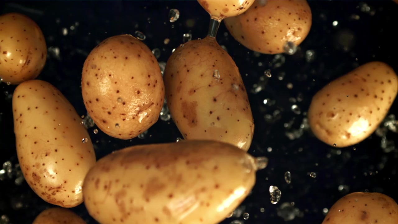 Patate fresche che schizzano con l'acqua al rallentatore su sfondo scuro