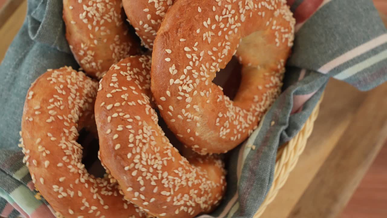 bagels dorados con semillas de sésamo giran sobre la mesa en una cesta tejida, vista de arriba hacia abajo