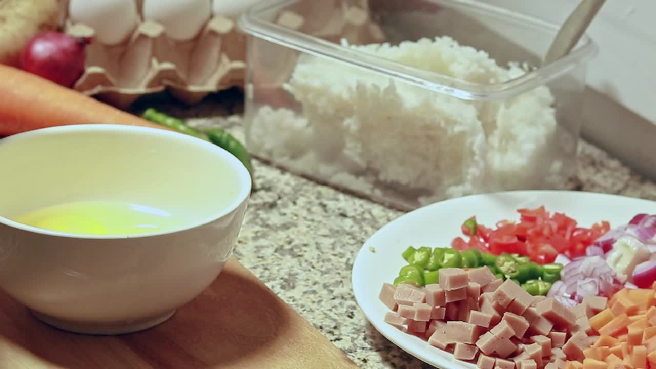 Candid kitchen scene of cracking an egg on a white bowl then beating it as part of the ingredient of a simple fried rice recipe
