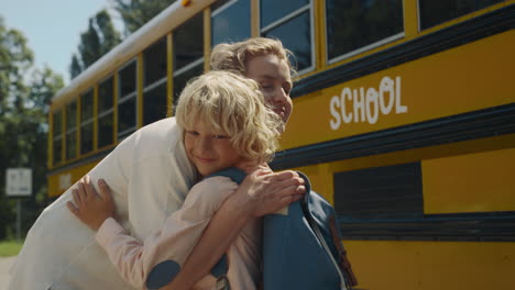 Smiling-mom-hugging-son-near-school-bus.-Boy-saying-goodbye-to-cheerful-mother.