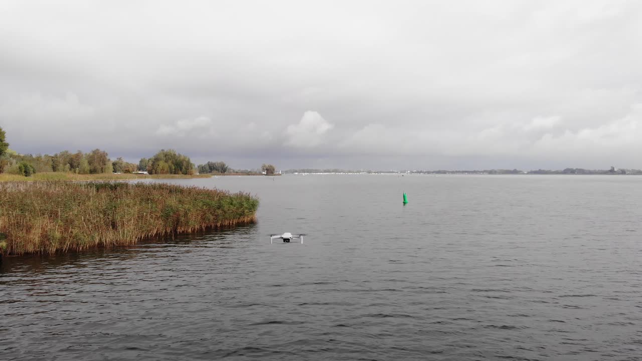 카메라가 오른쪽으로 이동하는 동안 호수 표면 위를 맴돌고 있는 작은 드론