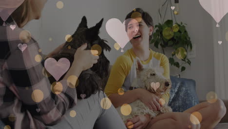 animación de corazones sobre pareja de mujeres caucásicas sentadas en el sofá con sus perros mascotas.