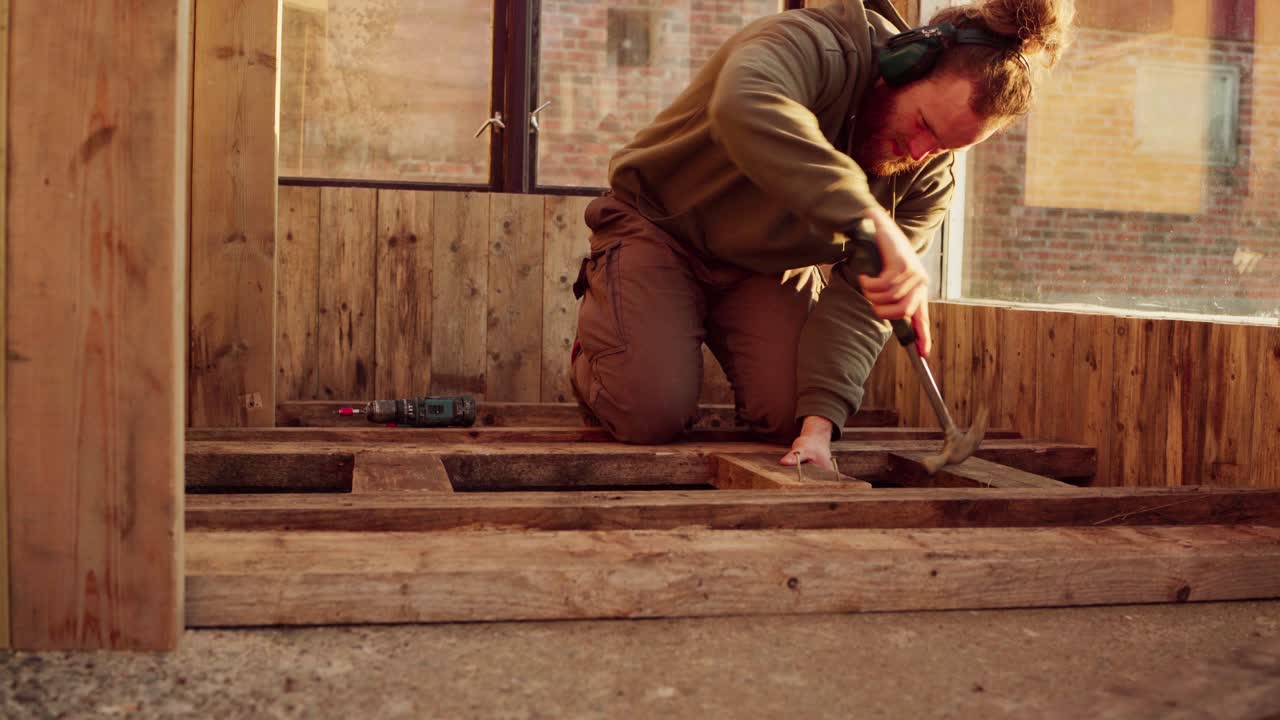 hombre martillando clavos en el soporte de madera del piso
