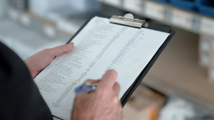 Hand with a pen makes notes on paper on a clipboard. Warehouse worker