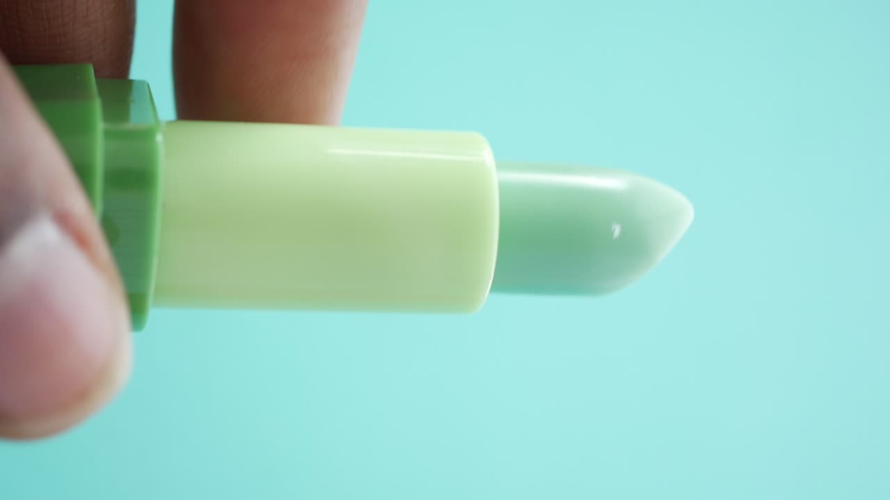 Close-up of a light green and mint-colored lip balm in hand