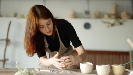 girl potter forms a ball from a piece of clay on the board