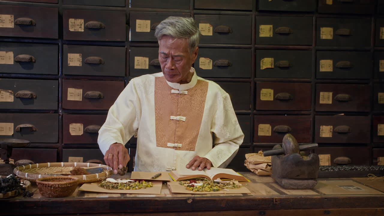 Aged Naturopath Writing Recipe at Table in Herbal Pharmacy