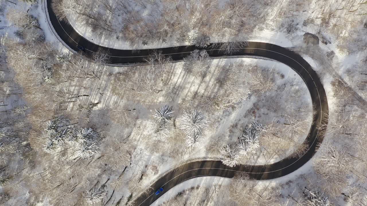 vista aérea de arriba hacia abajo en una carretera serpentina nevada con coches de conducción desde ambos lados - toma superior en invierno con árboles cubiertos de nieve que rodean la calle