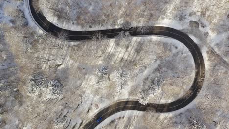 topdown aerial view at a snowy serpentine road with driving cars from both sides - top shot at the wintertime with snow covered trees surrounding the street