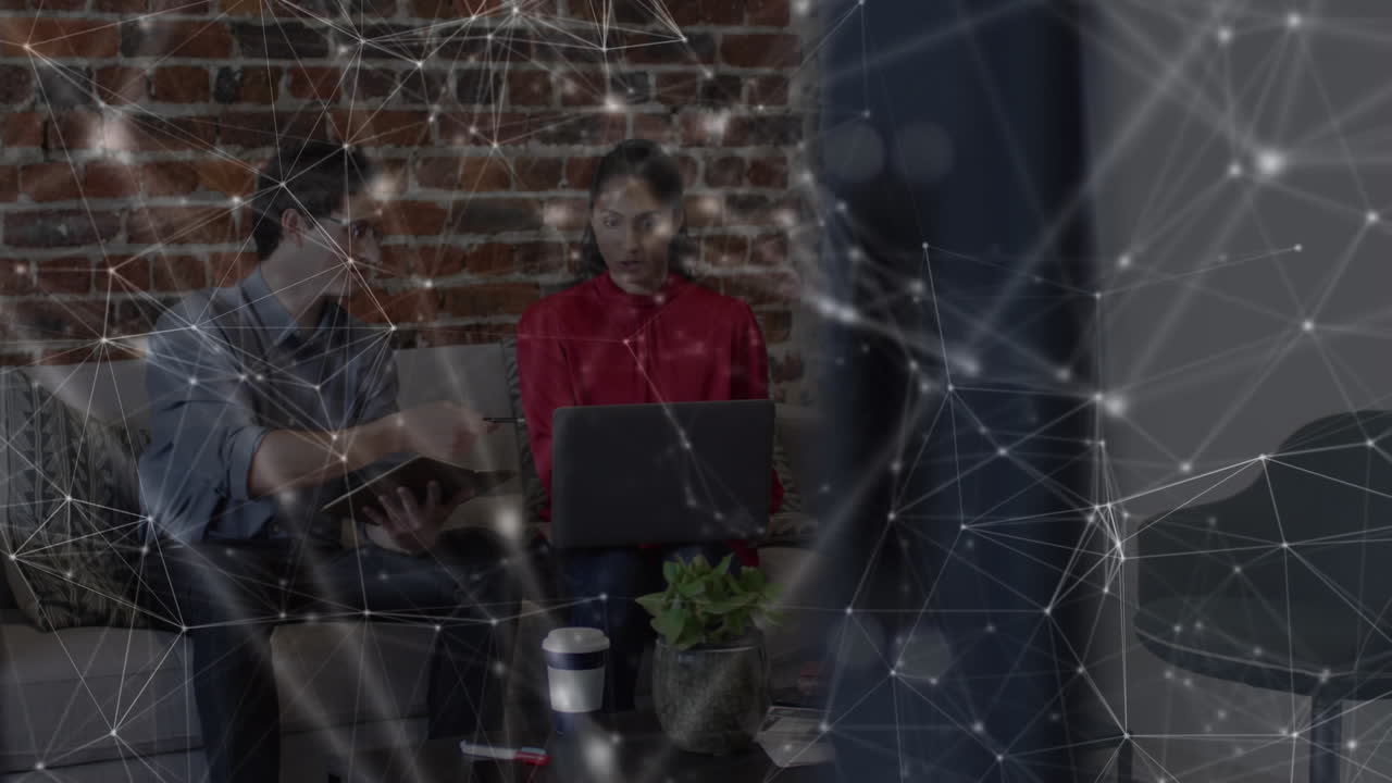Animation of network over male and female colleague using laptop on couch in office