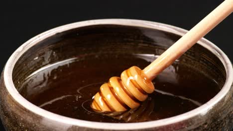 honey dripper is dipped to take honey in a bowl on the black background. honey dripping from honey dripper, healthy organic thick honey closeup, sweet honey dessert 4k. slow motion