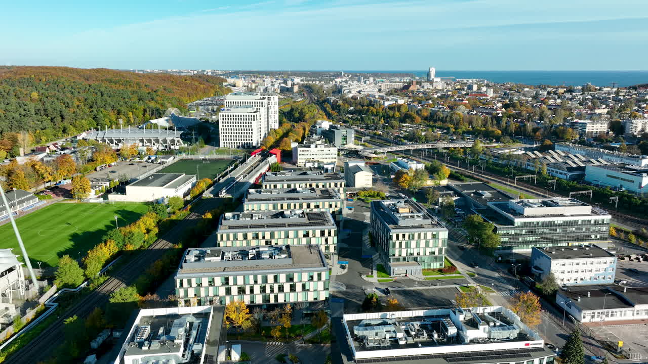 Aerial panorama of Gdynia with modern offices, stadium, and sea horizon visible in the distance on a sunny day