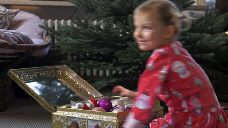 a young child opens a golden box with ornaments inside and smiles