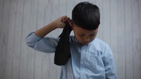 portrait of cute asian boy putting on his vest and fastened the button