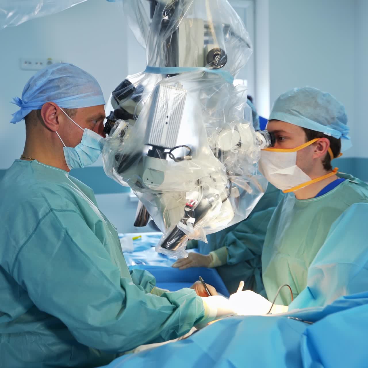 Professional team of two neurosurgeon perform operation on patient's arm. Gradual approaching to the surgeons sitting at big modern microscope