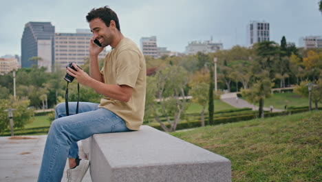 fotógrafo latino hablando teléfono inteligente en el parque verde. feliz tipo despreocupado llamando