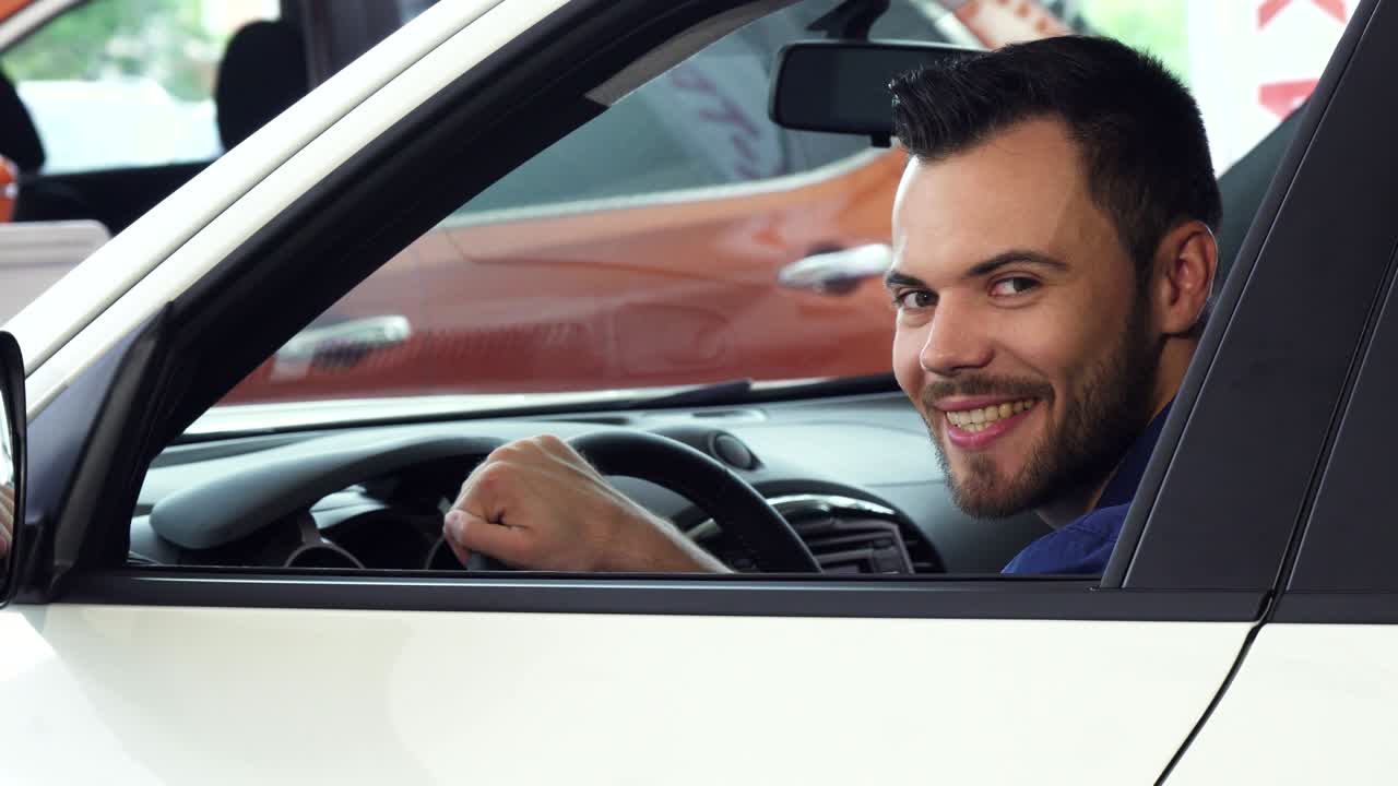 joven alegre y guapo sonriendo a la cámara sentado en su nuevo coche