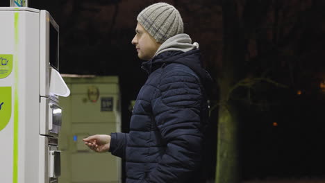 man lifts covering to insert credit card into machine while at gas service station at night