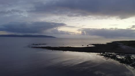 drone pullback above calm galway bay and barna pier reflecting sunset light at dusk