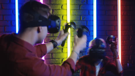 young man and woman in vr glasses and using joystick while playing a virtual reality game in a room with colorful neon lamps on the wall 3