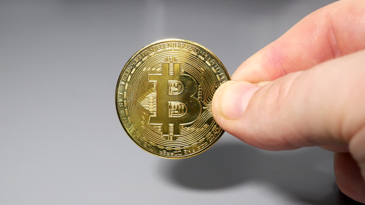 moneda bitcoin de oro sostenida entre los dedos en la mano en la mesa gey