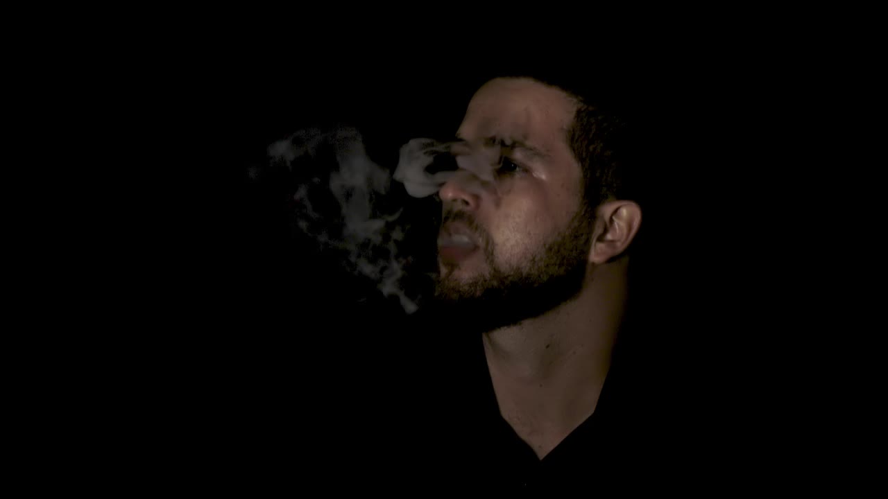 hombre guapo de pie en el estudio y vapeando con cigarrillo electrónico