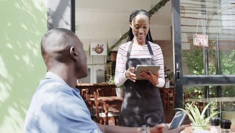 Barista-Afroamericana-Con-Tableta-Tomando-El-Pedido-Del-Cliente-Fuera-De-La-Cafetería,-Cámara-Lenta