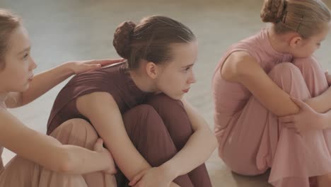 검은색 댄스웨어를 입은 젊은 발레 학생들이 나무 바닥과 벽에 장착된 바를 가진 넓은 발레 스튜디오에서 자세를 연습하는 그룹.