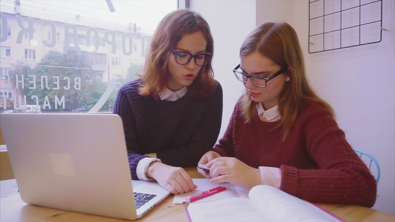 dos mujeres jóvenes estudiando juntas en un café