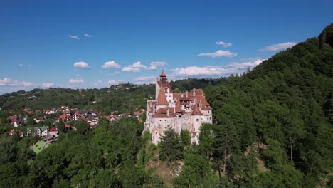 scenic aerial shot orbiting around bran castle, showcasing its medieval architecture, nestled among the green hills and forests of transylvania.