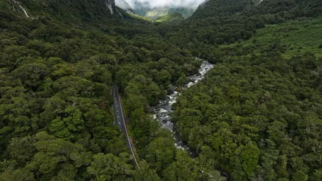 Luftaufnahme-Dolly-über-Straße-Schlängelt-Sich-Entlang-Rocky-River-An-Der-Talsohle-In-Milford-Sound