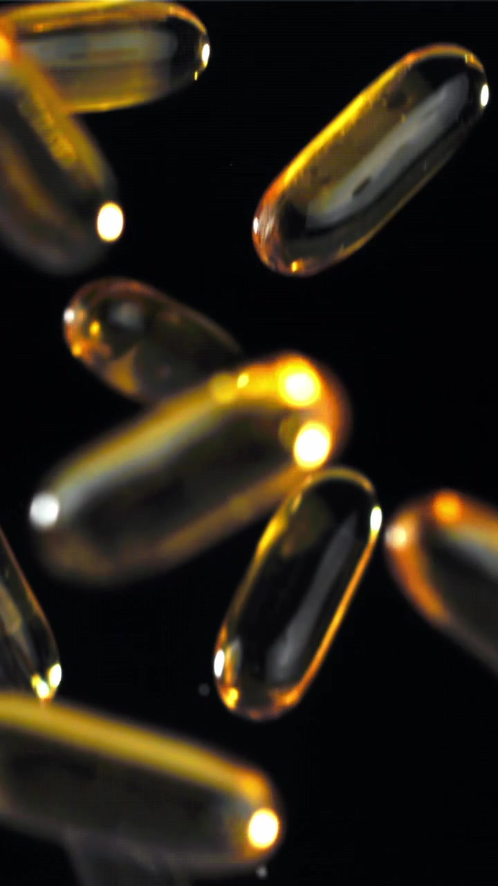 Capsule softgel dorate che cadono al rallentatore su sfondo nero