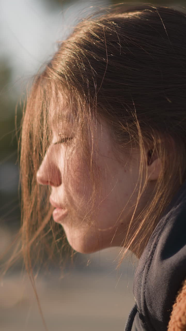 A close-up of a girl wearing a brown coat, with her hair partially covering her face. She looks mournful and lost in thought, her expression reflecting a profound sense of sadness and contemplation