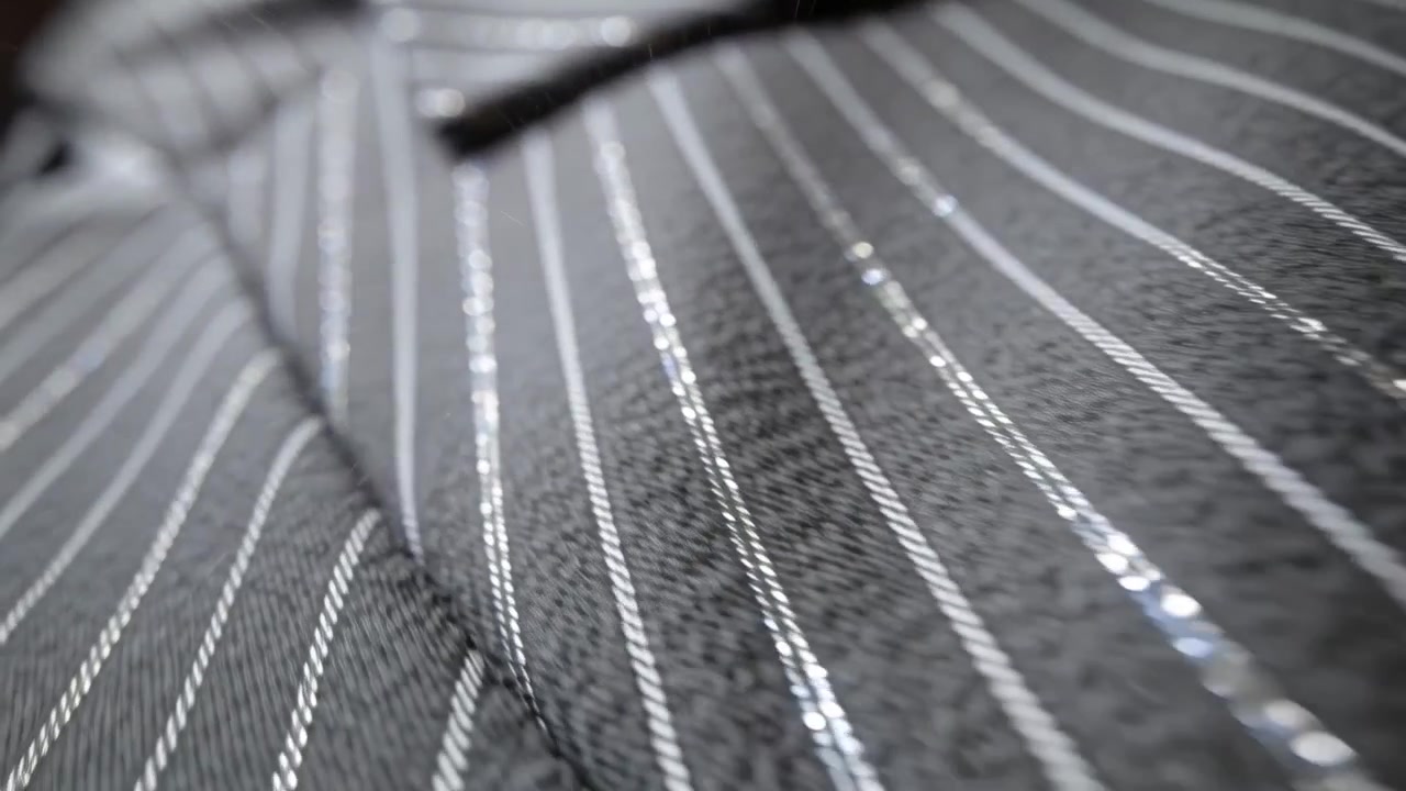 Gros plan montrant le tissu d'une veste de costume bougeant avec le mouvement de la caméra, révélant une couture à fines rayures argentées.