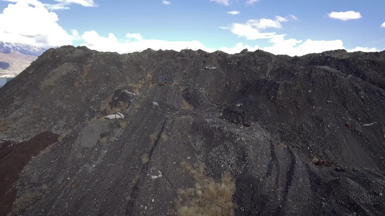 A drone flies up and over a giant slag heap mountain to reveal a reflective catch pond, leftover remnants from the Geneva Steel steel mill.