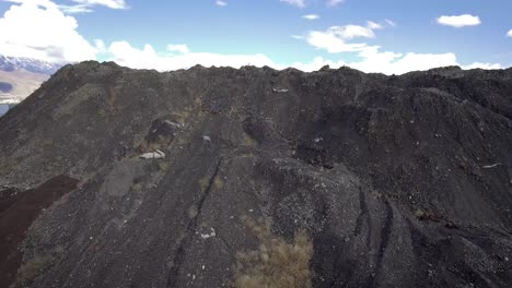 a drone flies up and over a giant slag heap mountain to reveal a reflective catch pond, leftover remnants from the geneva steel steel mill.