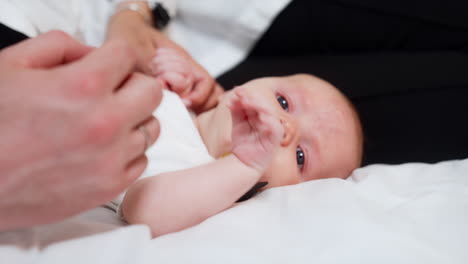 Adorable Caucasian newborn lies holding a pacifier in mouth. Mother holds baby's hands and kid drops the pacifier. Close up.
