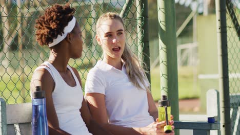 video of happy diverse female tennis players sitting, talking and resting after match