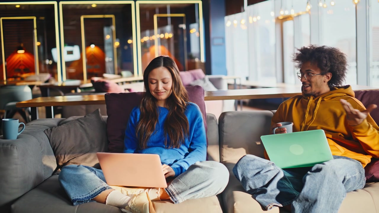 Multiracial team working laptop coworking lounge. Man talking coffee mug sofa.