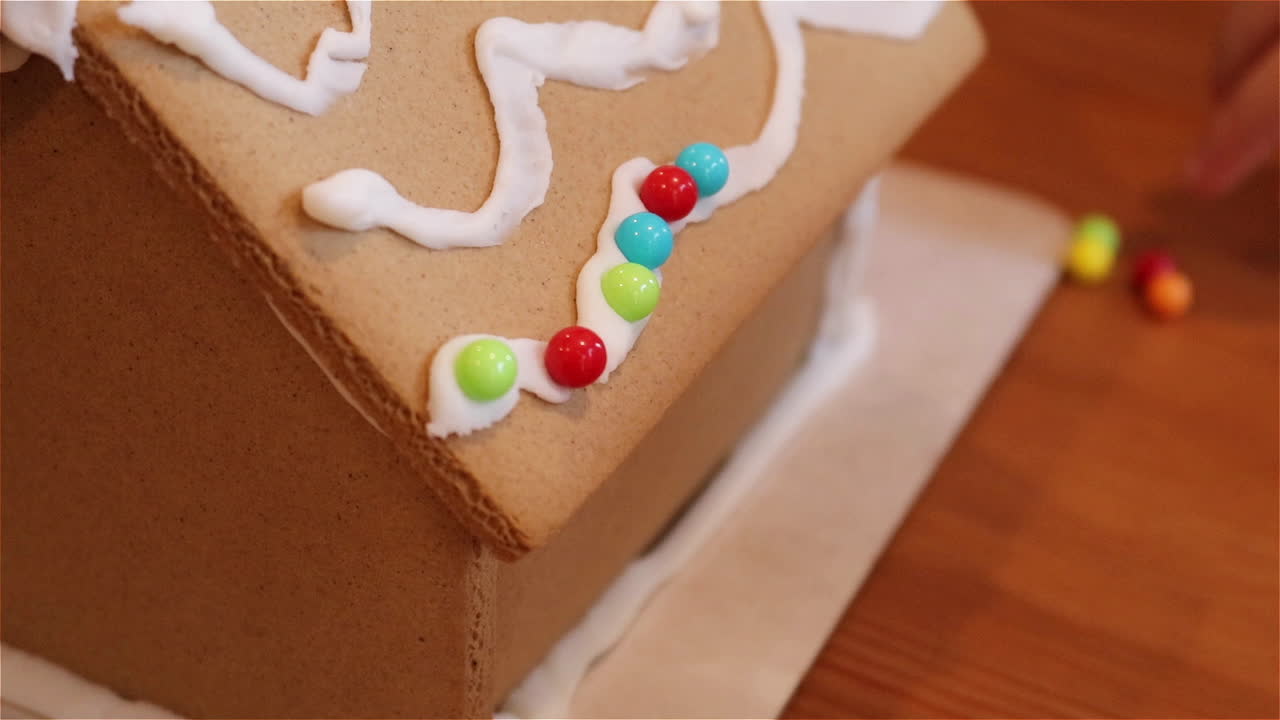 Young child adds candies to a row of icing on a gingerbread house
