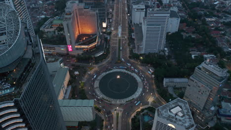Aerial-tilting-horizontal-to-overhead-view-of-a-busy-traffic-on-a-Selamat-Datang-Monument-roundabout-surrounded-by-modern-skyscrapers-in-Jakarta,-Indonesia
